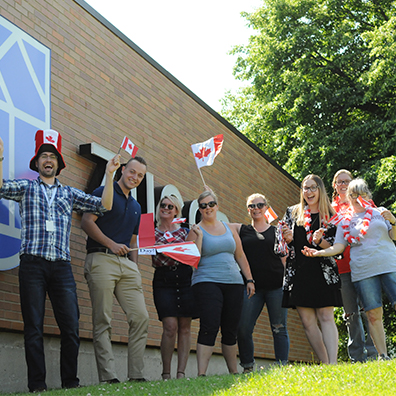 Employees standing near ZucoraHome name board with Canada day flags and props.